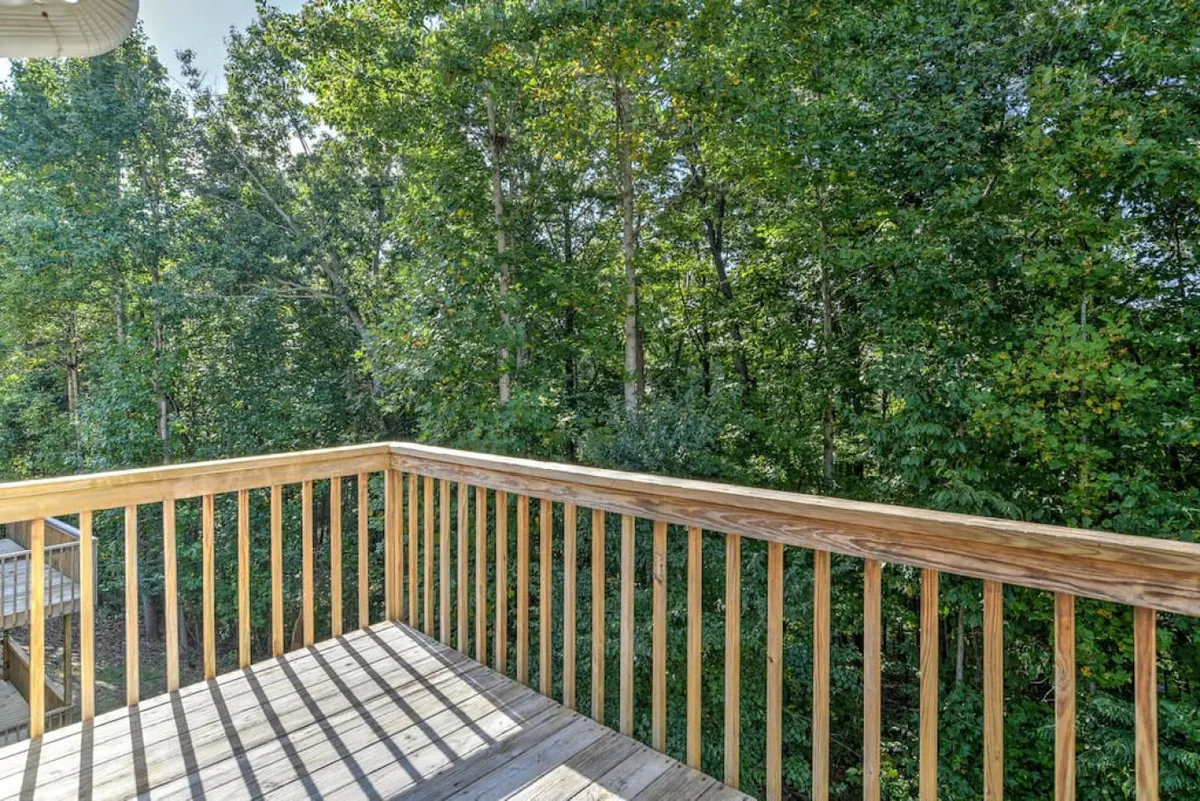 This image captures a peaceful outdoor deck surrounded by lush green trees, with a sturdy wooden railing and attractive deck flooring. The space invites guests to relax and soak in the natural setting, offering a serene connection to the outdoors.