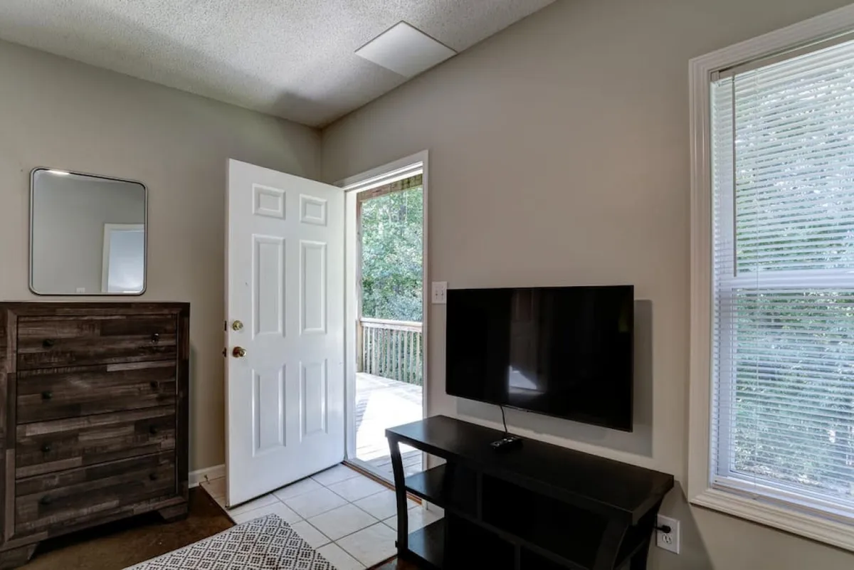 A welcoming interior scene featuring an open door leading outside, a TV, a comfortable dresser, and bright windows. The open door symbolizes easy transitions between the home and the surrounding area, while the inviting seating area suggests a space to gather after a day of exploration.