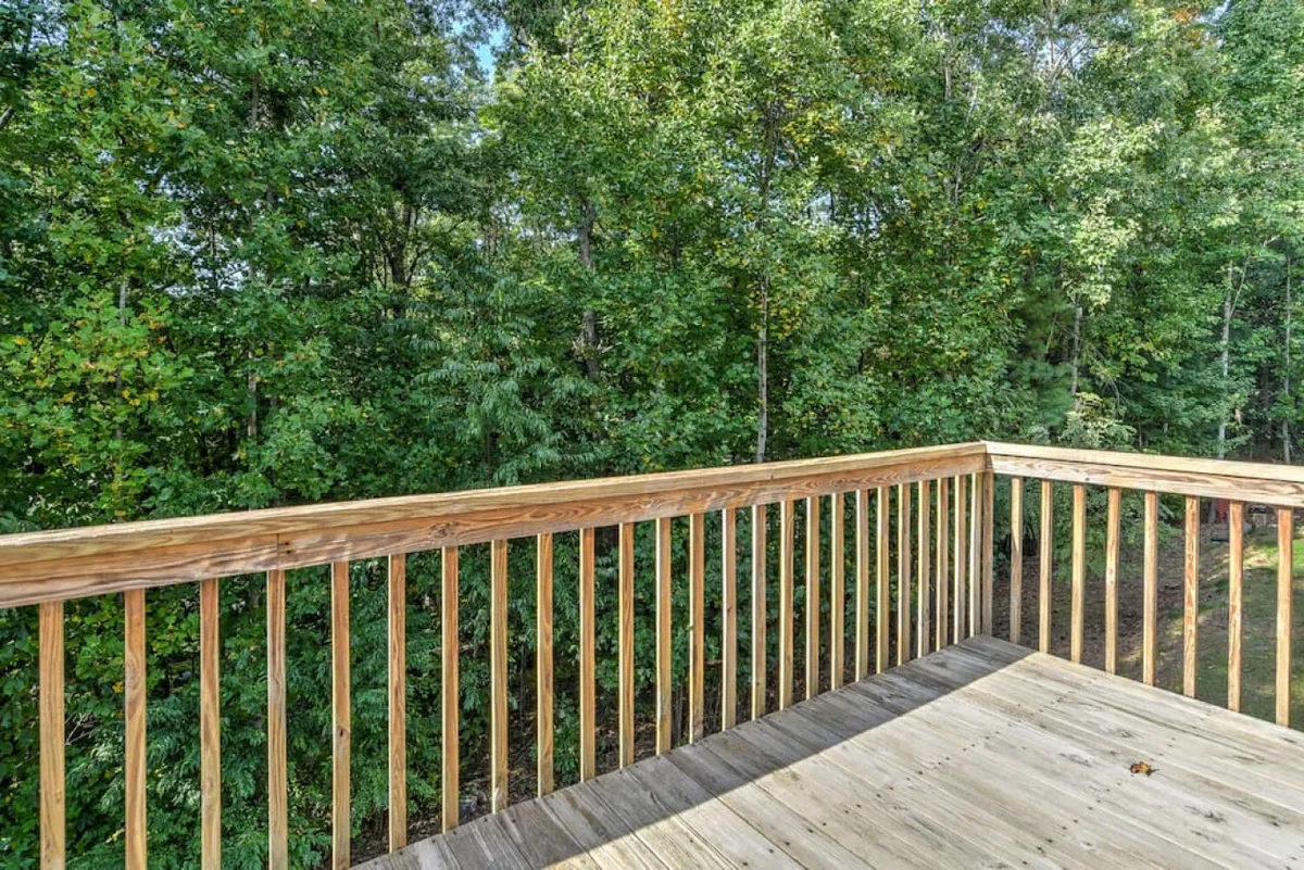 A tranquil wooden deck framed by a sturdy railing, surrounded by lush green trees. The scene is peaceful, with soft natural light filtering through the foliage, inviting you to step outside for a quiet morning or an afternoon break. The space suggests a private, open-air retreat perfect for enjoying fresh air and the sights and sounds of nature.